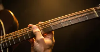 Nahaufnahme einer E-Gitarre im warmen Licht, mit Fokus auf Saiten und Händen beim Spielen. Die Szene wirkt ruhig, konzentriert und nachdenklich.
